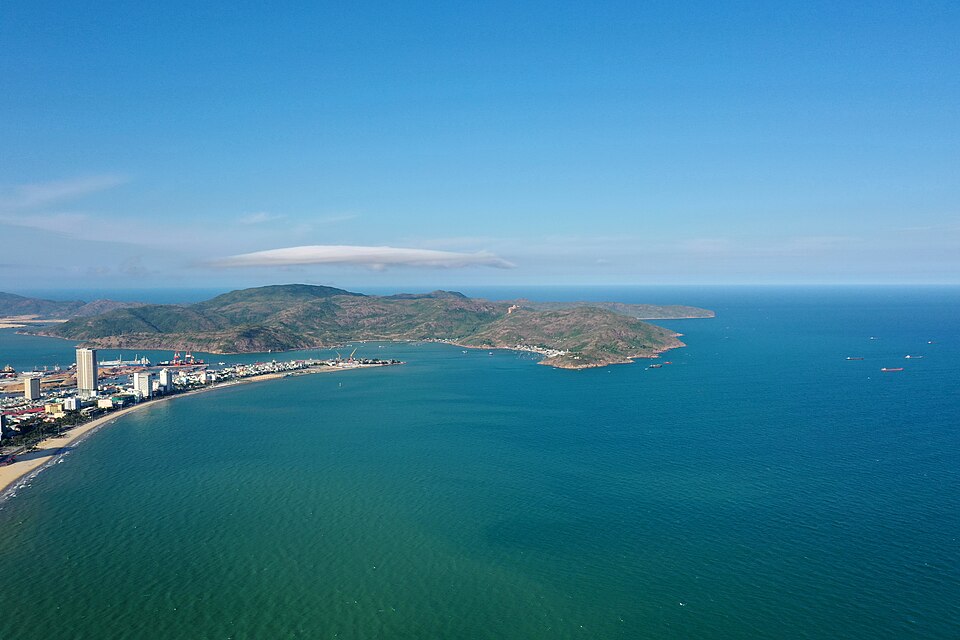 Aerial view of Quy Nhon’s waterfront and blue coastal waters, with Phuong Mai Peninsula in the distance.