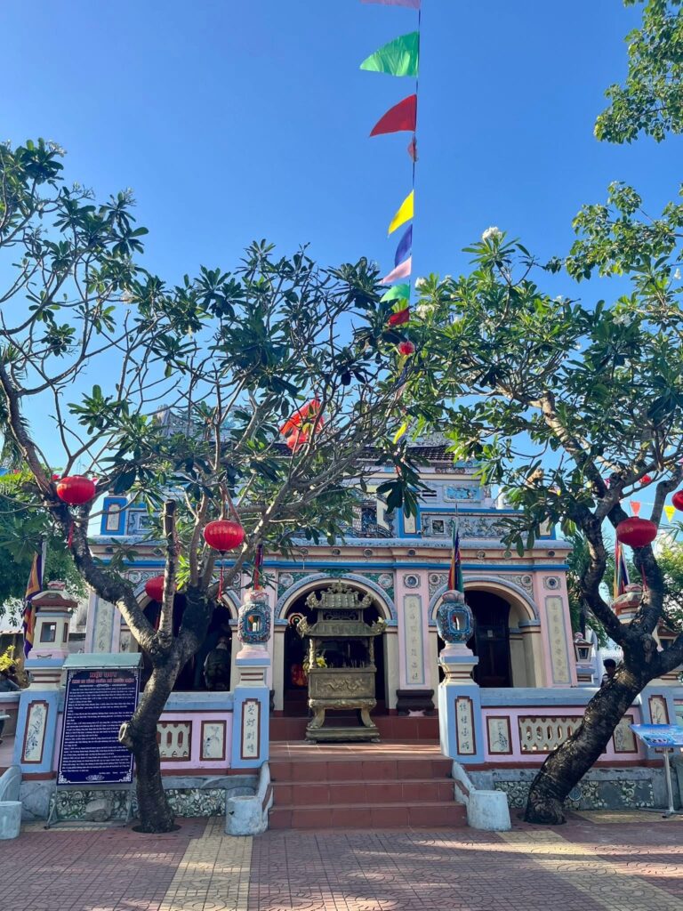 Front view of Nuoc Man Temple, showing three arched doorways, an ornate incense burner and red lanterns.